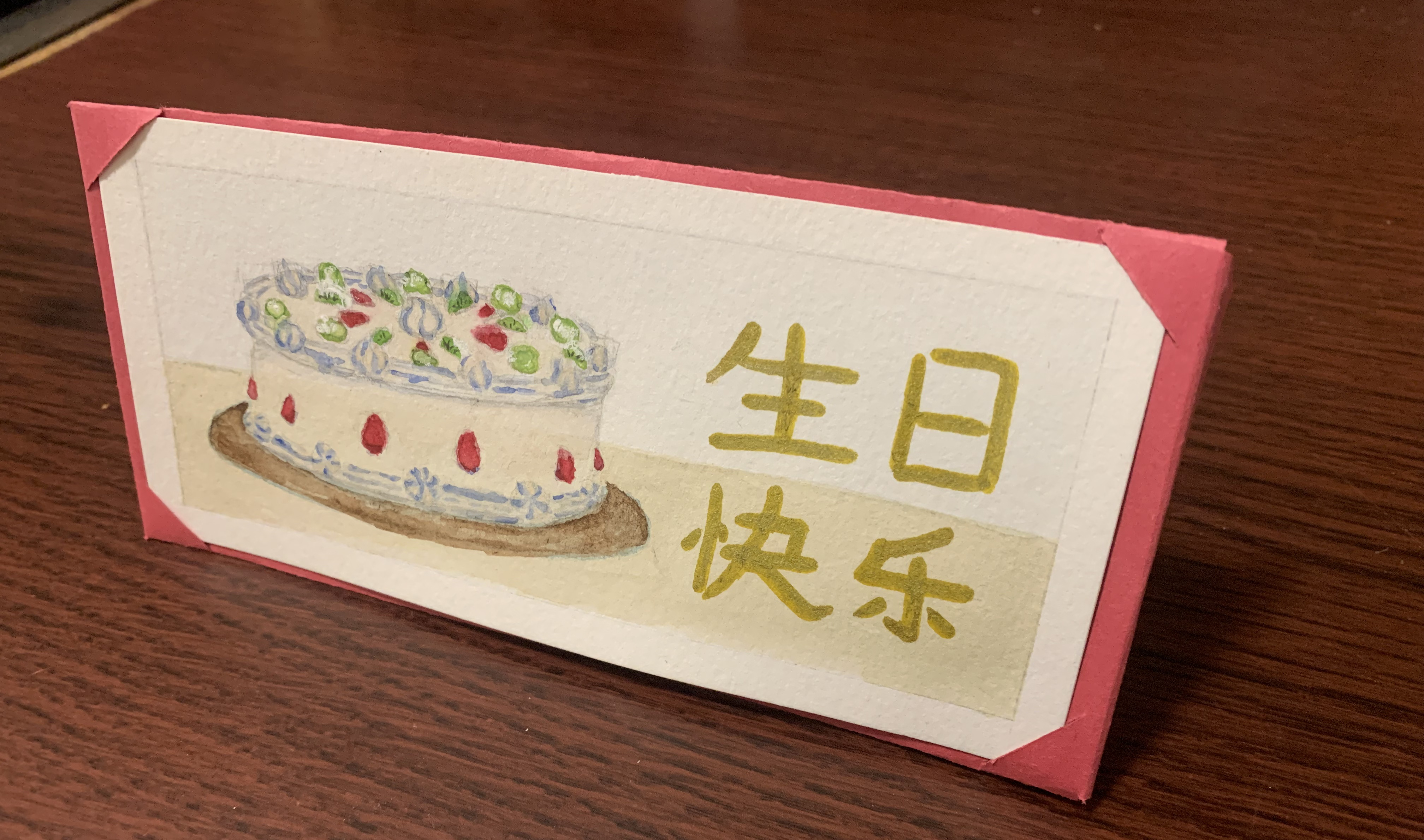 a watercolor painting of a Chinese fruit cake: iced with whip cream and a chinese phrase which translates to[Happy Birthday] written in gold marker